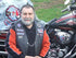 man wearing an orange and black sweat shirt and vest in front of red and black Harley Davidson motorcycle